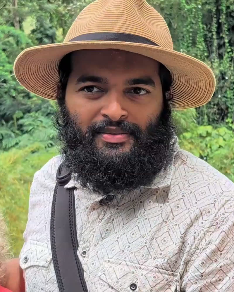 Ra Netjer in a wide-brimmed hat, smiling, in the Hawaiian rainforest